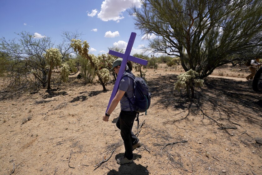 Alyssa Quintanilla, part of the Tucson Samaritans volunteer group, carries a cross Tuesday, May 18, 2021, to be installed at the site of the migrant who died in the desert some time ago, in the desert near Three Points, Ariz. Protecting migrants and honoring the humanity of those who died on the perilous trail is a kind of religion in southern Arizona where spiritual leaders four decades ago founded the Sanctuary Movement, a campaign to shelter Central Americans fleeing civil war, and scores of volunteers carry on their legacy today. (AP Photo/Ross D. Franklin)
