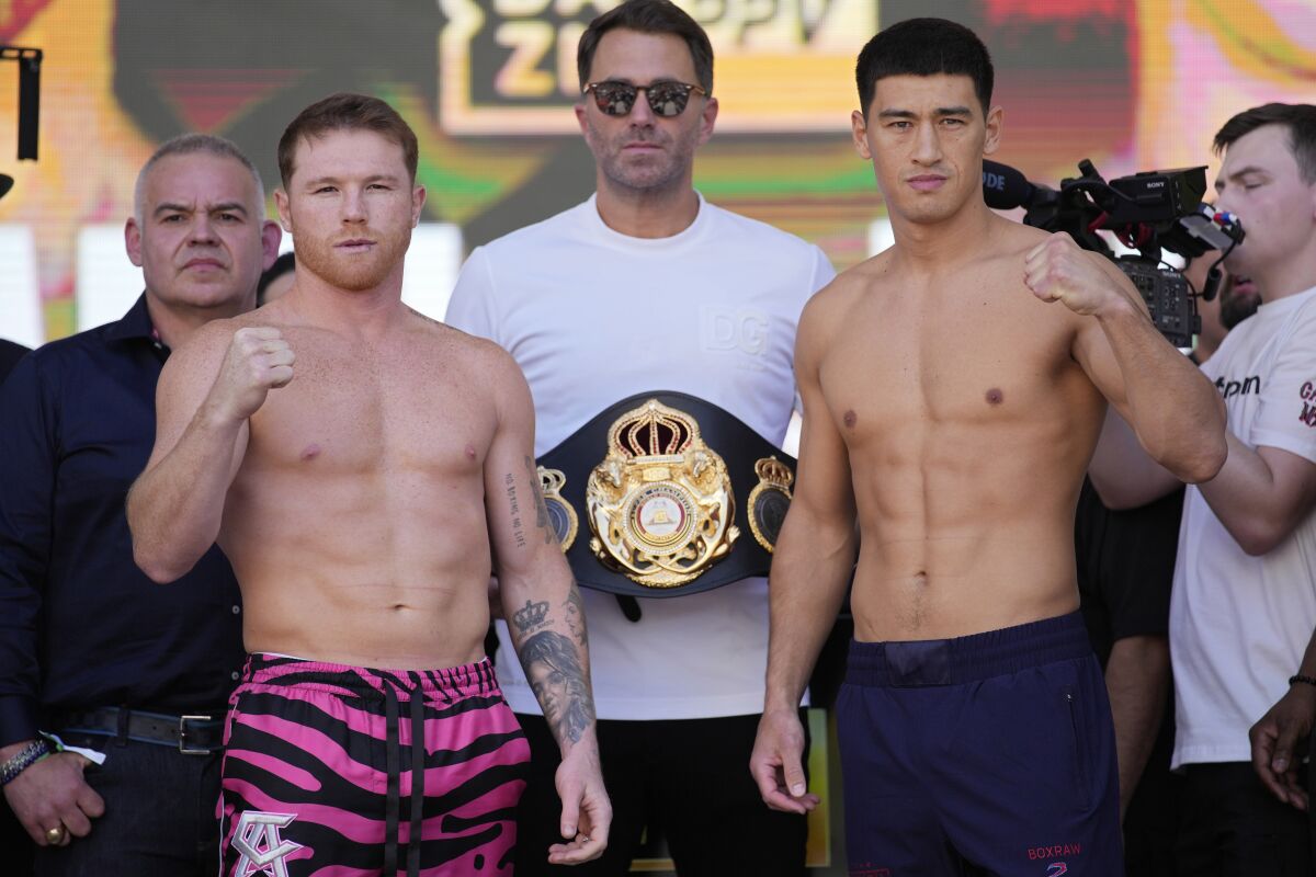 Canelo Álvarez stands next to Dmitry Bivol and Eddie Hearn during a weigh-in 