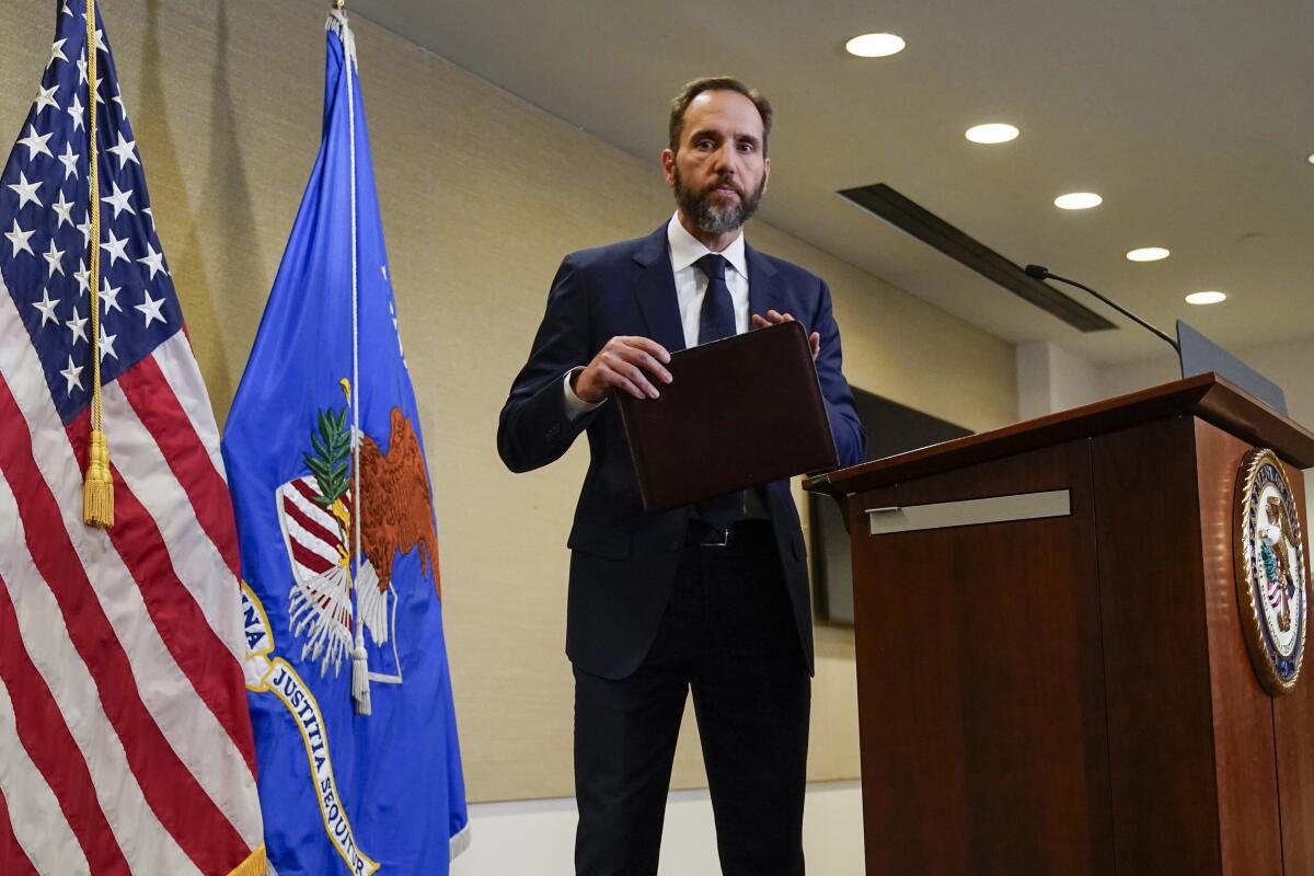 Special counsel Jack Smith holding a folder as he  stands between a lectern and the American and Justice Department flags
