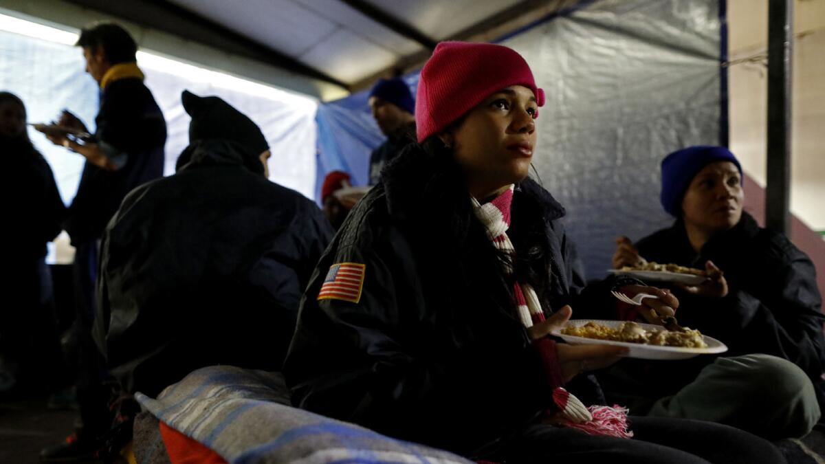 MATAMOROS, TAMAULIPAS -- MONDAY, NOVEMBER 12, 2018: Jessica Zamora, 18, of Havana, Cuba, who is pregnant, seeking political asylum, eats a meal prepared by Brendon Tucker, 23, of Canyon Lake, Texas, while camping along with other immigrants outside Mexicos' National Institute of Migration office at the Gateway International Bridge in Matamoros, Tamaulipas, on Nov. 12, 2018. Volunteers from the U.S. feed immigrants seeking asylum who are camping out along the U.S. - Mexico border at the Gateway International Bridge in Matamoros, Tamaulipas. (Gary Coronado / Los Angeles Times)