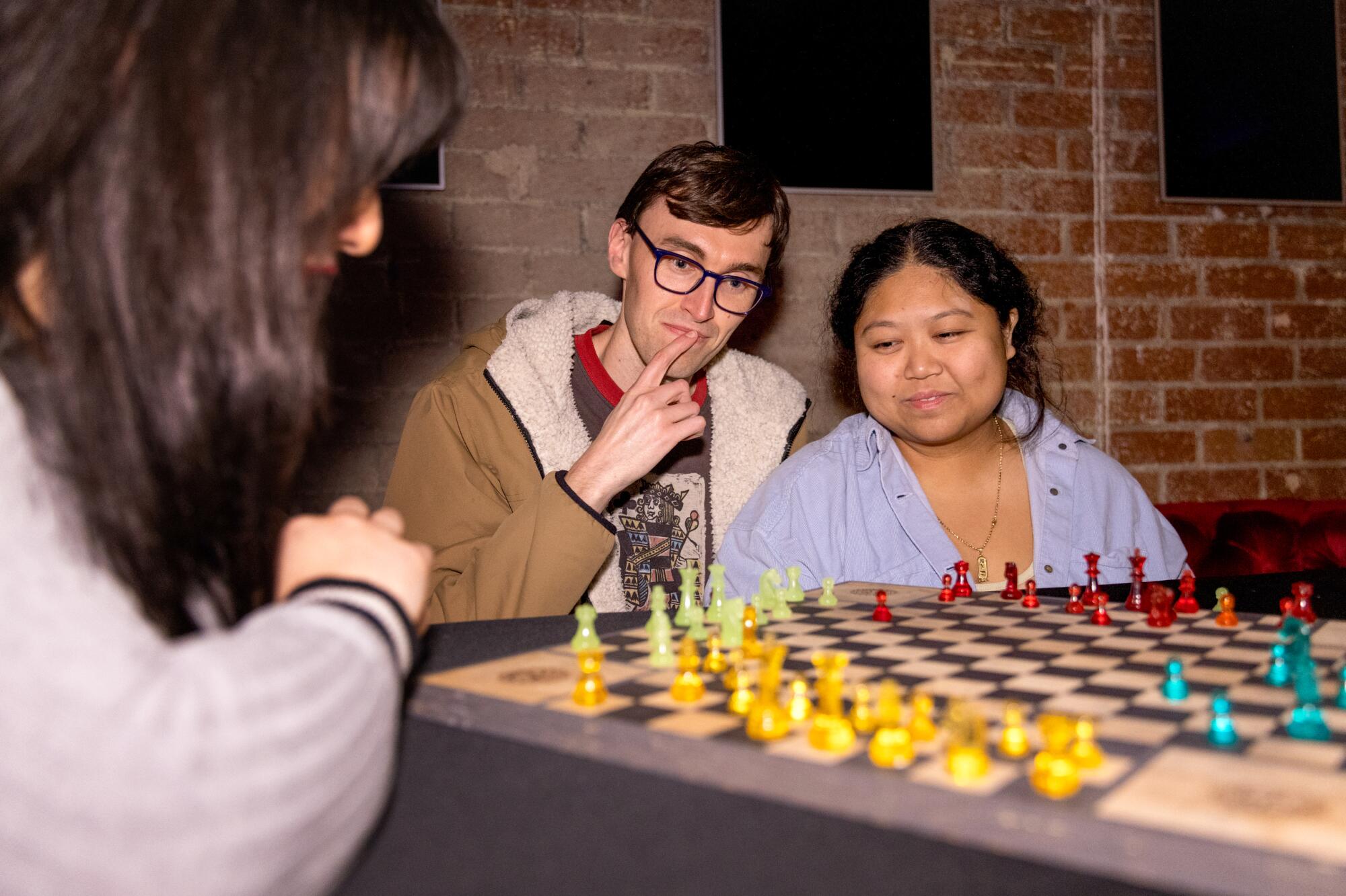 Three people play chess together on a multi-player board.