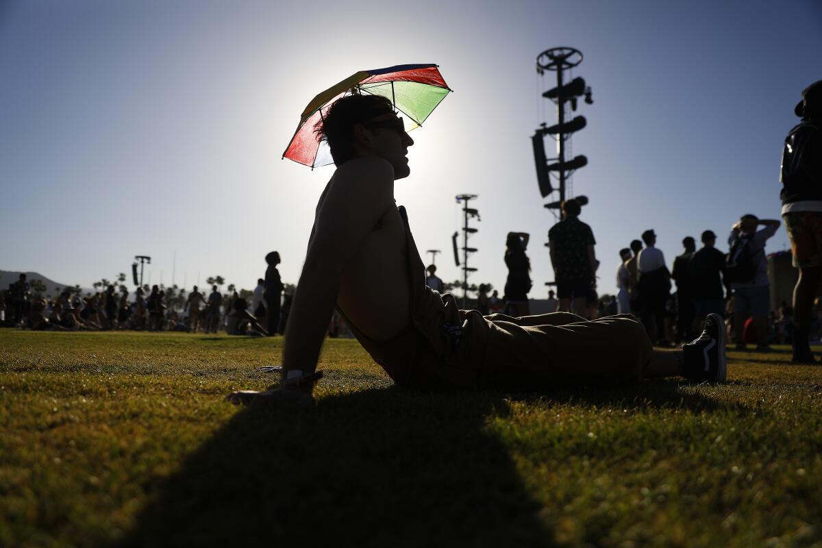 Fan wearing an umbrella hat sits on the ground at Coachella 2022