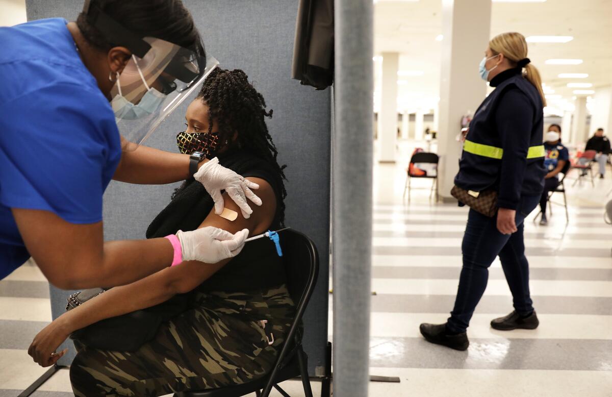 A health worker with a face shield puts a Band-Aid on a woman after giving her a vaccination.