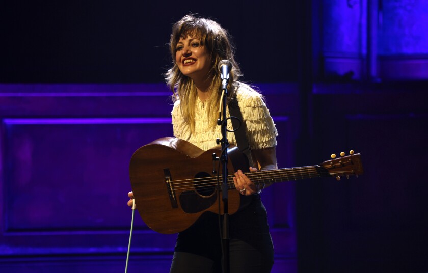 Anaïs Mitchell en el escenario, sonriendo y sosteniendo una guitarra.