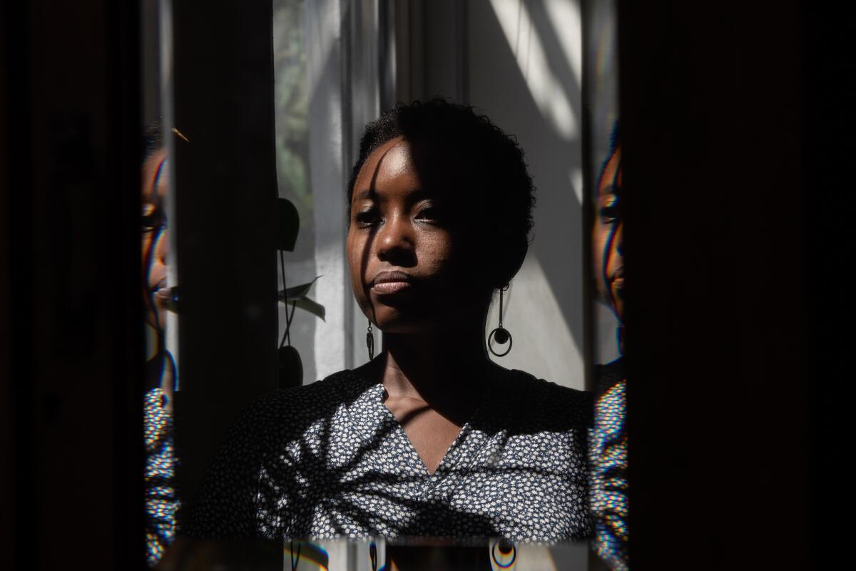 Zakiya Dalila Harris, with a shadow cast over the left side of her face, looking out the window of her Brooklyn apartment.
