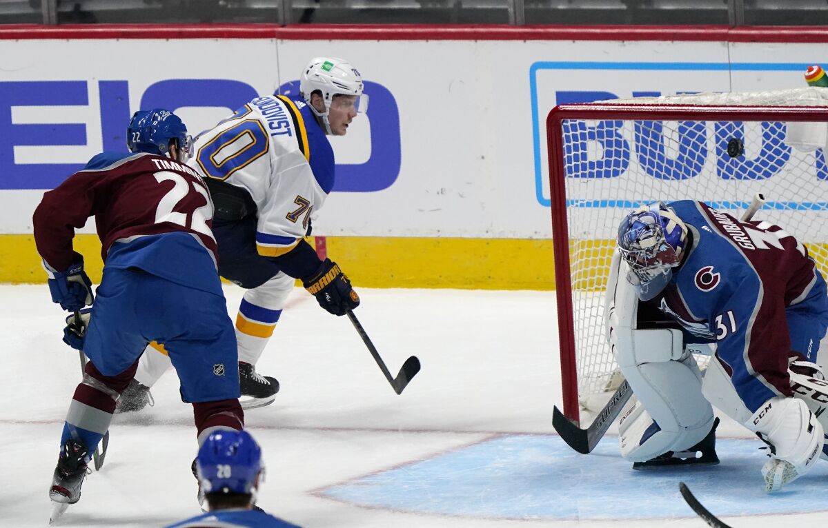 St. Louis Blues center Oskar Sundqvist, back, drives past Colorado Avalanche defenseman Conor Timmins, left, to score a goal against goaltender Philipp Grubauer in the third period of an NHL hockey game Wednesday, Jan. 13, 2021, in Denver. The Blues won 4-1. (AP Photo/David Zalubowski)