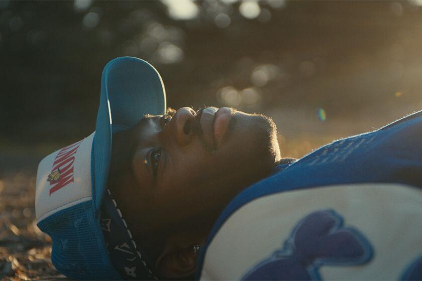 Lil Nas X laying on the ground in a blue and white hat and sweatshirt.