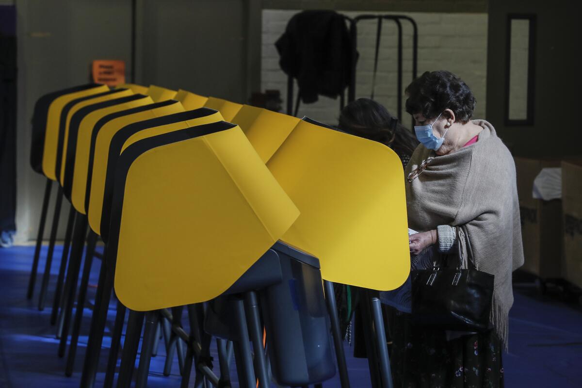 A woman in a mask at a voting booth.