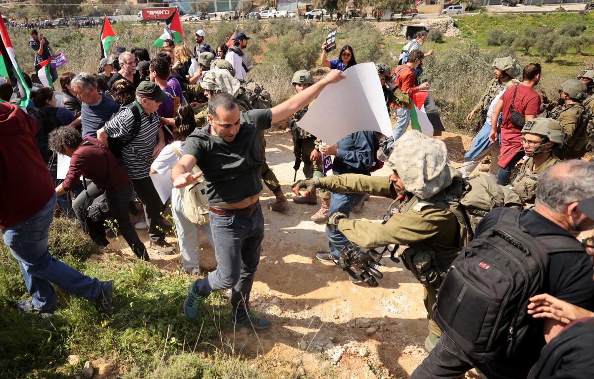 Protesters with Palestinian flags clash with security forces on a hill.