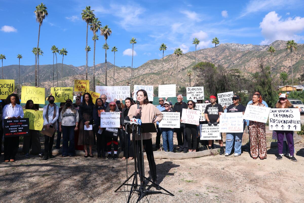 Kara Vallow speaks on the site of her former home while standing in front of several people holding signs