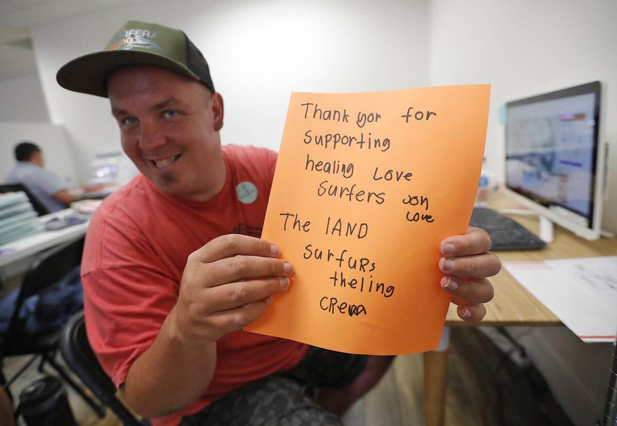 Jonathan Guinn shows the thank-you cards given to online order clients for Surfers Healing at Zuggy Etc. work space.