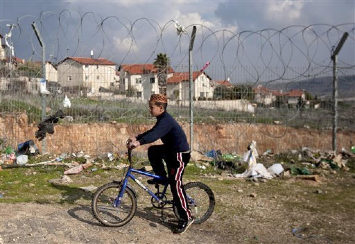 In this photo taken Wednesday, Feb. 9, 2011 a Palestinian boy rides his bicycle outside the fenced-in house of al-Ghirayim family between the Jewish settlement of Givon Hahadasha and the West Bank village of Beit Ijza. The al-Ghirayib family lives in one of the stranger manifestations of Israel's 43-year occupation of the West Bank: a Palestinian house inside a metal cage inside an Israeli settlement. The family's 10 members, four of them children, can only reach the house via a 40-yard (meter) passageway connecting them to the Arab village of Beit Ijza below. The passage passes over a road frequented by Israeli army jeeps and is lined on both sides with a 20-foot-high (6-meter) heavy-duty metal fence.(AP Photo/Sebastian Scheiner)