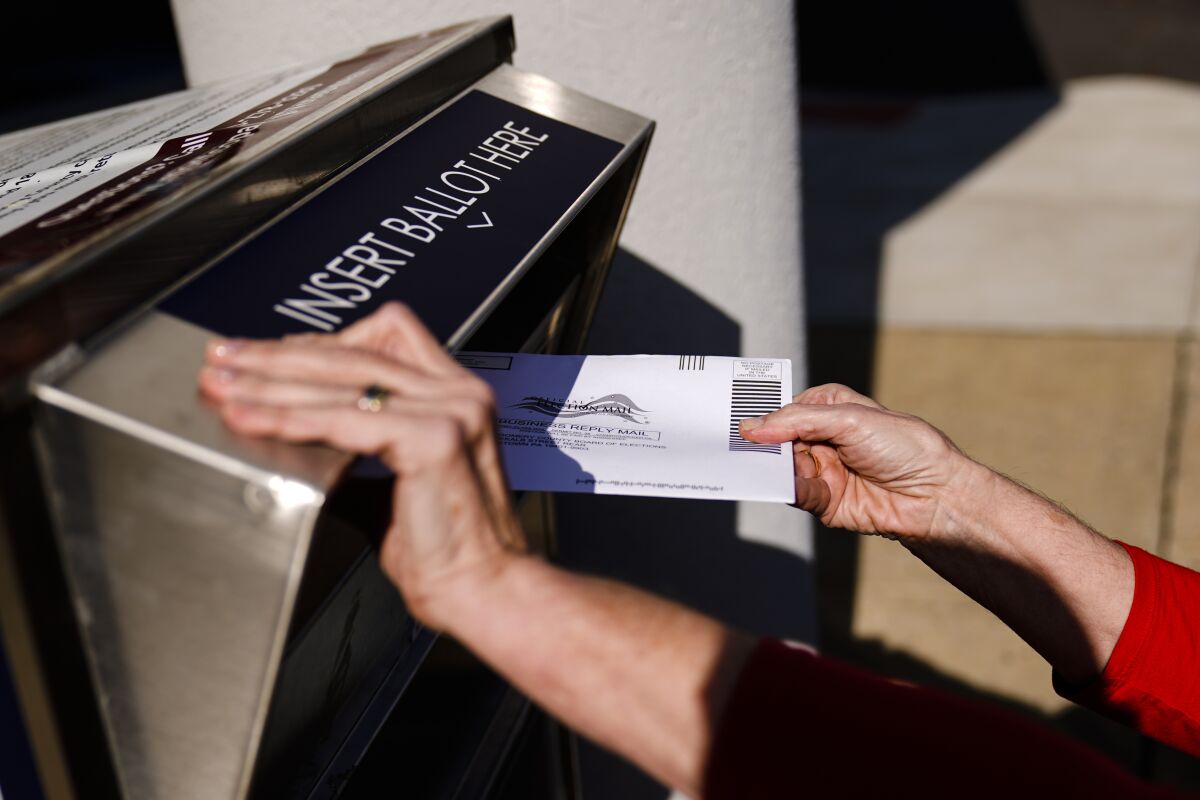 A person drops a mail-in ballot into a metal election ballot return box.