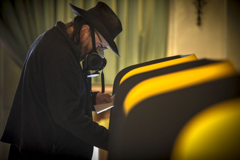 AZUSA, CA - OCTOBER 24: Jon, who gave only first name, in full face mask works on his ballot at In-person early voting place at Azusa Women's Club on Saturday, Oct. 24, 2020 in Azusa, CA. (Irfan Khan / Los Angeles Times)