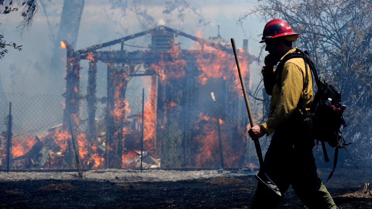 A firefighter walks by an empty burning structure near Irvine Lake during a brush fire Monday.