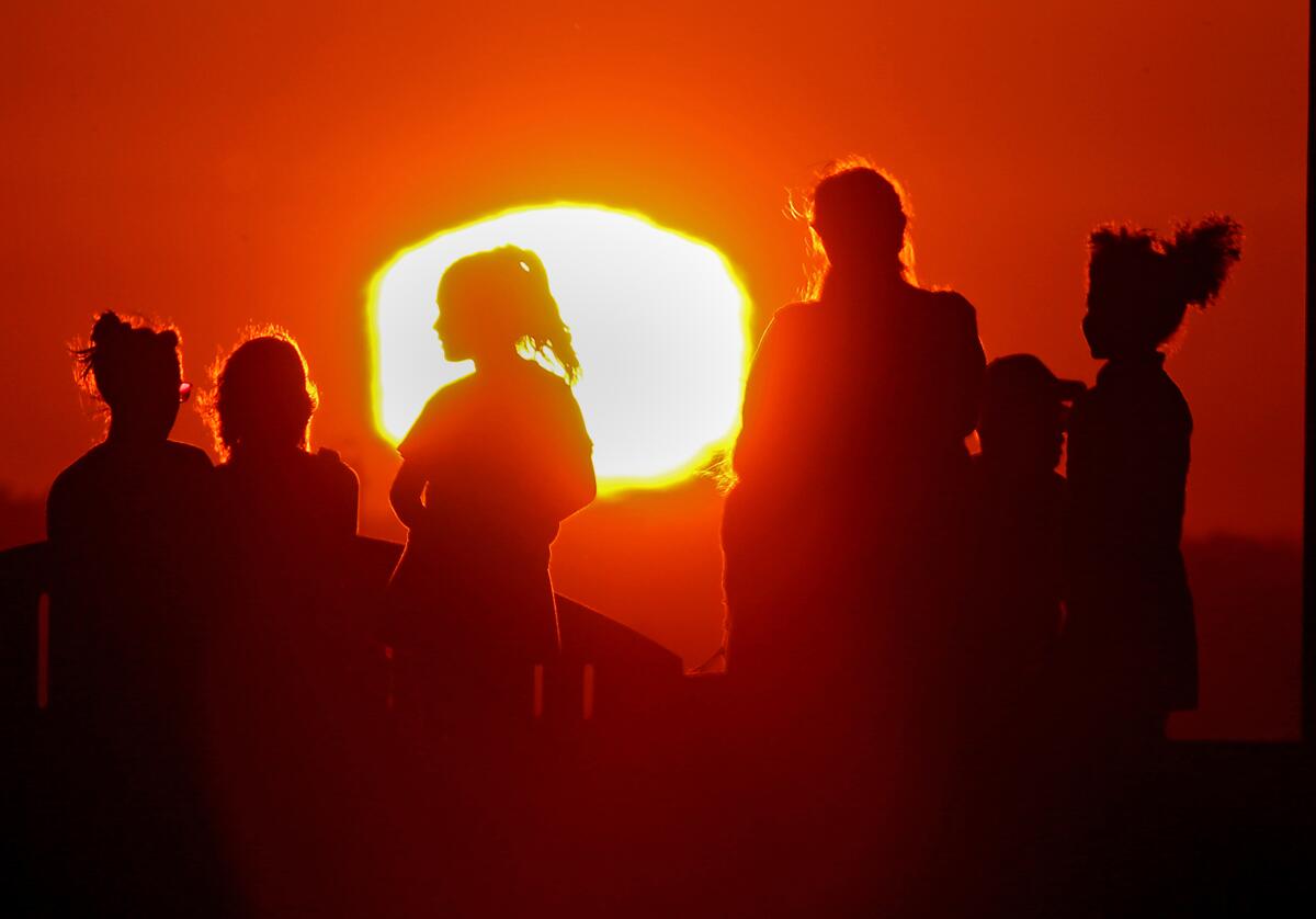 The outline of six people is seen against a red sky and bright yellow sun.