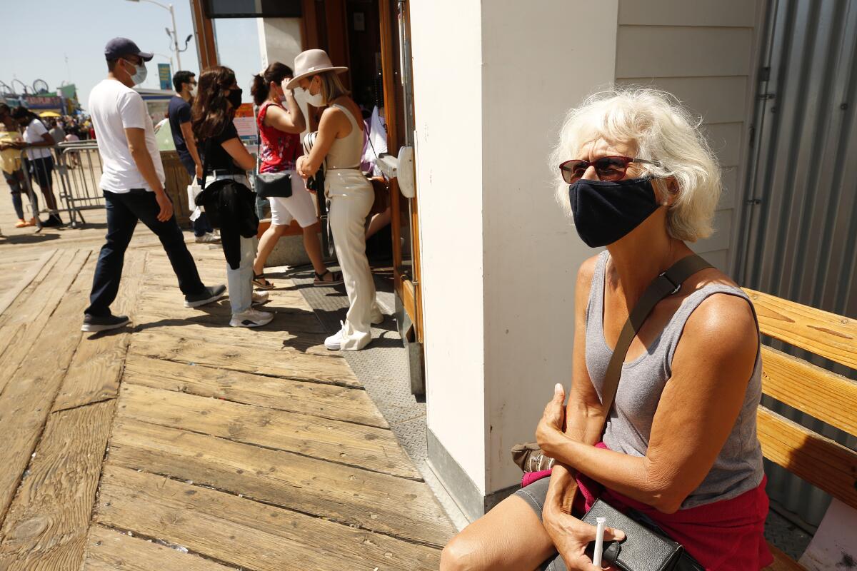 A woman wears a mask while sitting on the Santa Monica Pier.