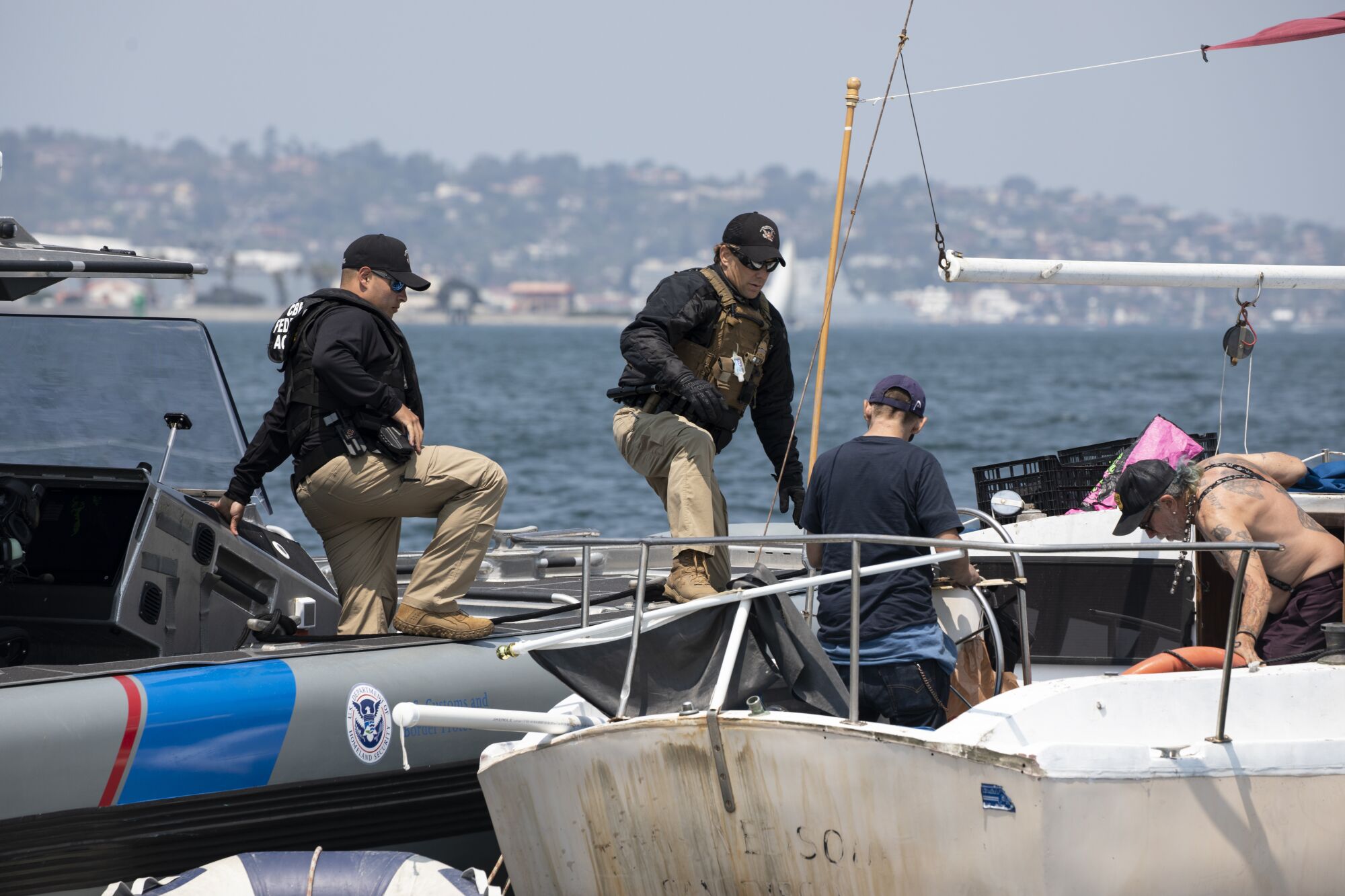 Marine interdiction agents board a sailboat from their boat after stopping the vessel.