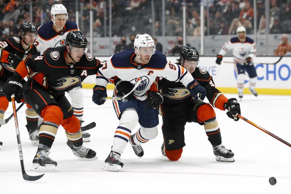 Edmonton Oilers center Connor McDavid, center, races for the puck with Anaheim Ducks defenseman Cam Fowler (4) and defenseman Jamie Drysdale, right, during the first period of an NHL hockey game in Anaheim, Calif., Sunday, April 3, 2022. (AP Photo/Alex Gallardo)