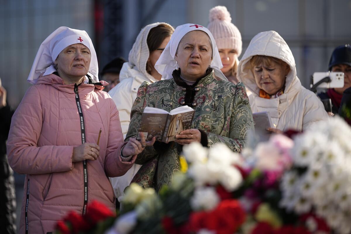 Women pray next to a display of flowers.