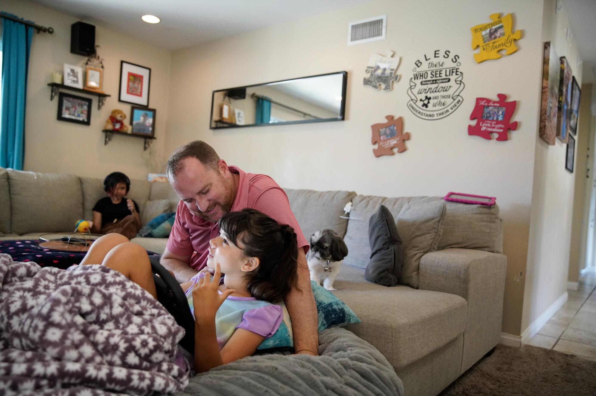 A dad talks to his daughter on a bean bag chair while another daughter sits on a couch.