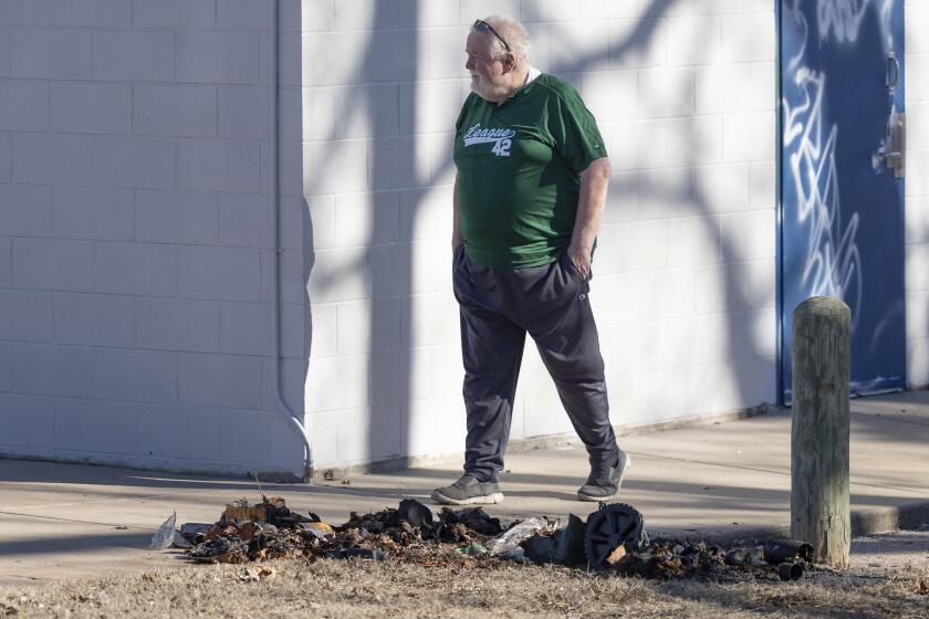 Bob Lutz walks past the charred remains of a dumpster 