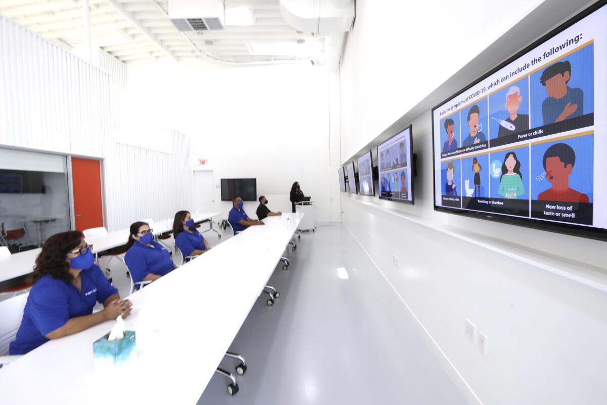 Workers watch video screens in a conference room.