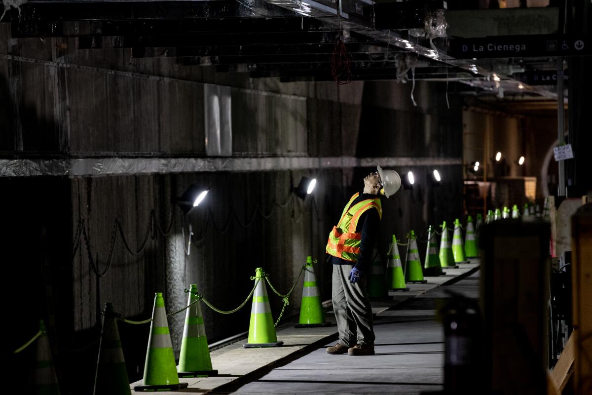 Un travailleur en équipement de sécurité orange se tient près d'une série de cônes de sécurité lumineux dans un tunnel sombre, levant les yeux