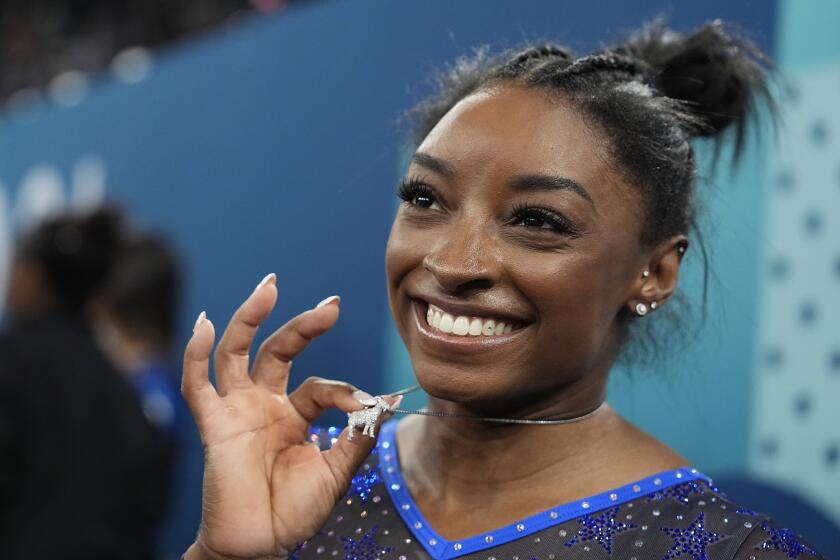 Simone Biles holds up her goat necklace and grins after winning the women's gymnastics all-around finals