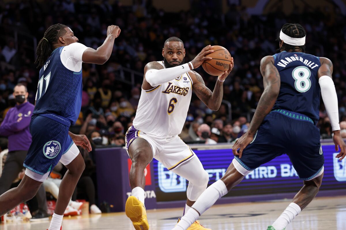 Los Angeles Lakers forward LeBron James (6) drives between Minnesota Timberwolves center Naz Reid (11) and Jarred Vanderbilt (8) during the first half of an NBA basketball game in Los Angeles, Sunday, Jan. 2, 2022. (AP Photo/Ringo H.W. Chiu)