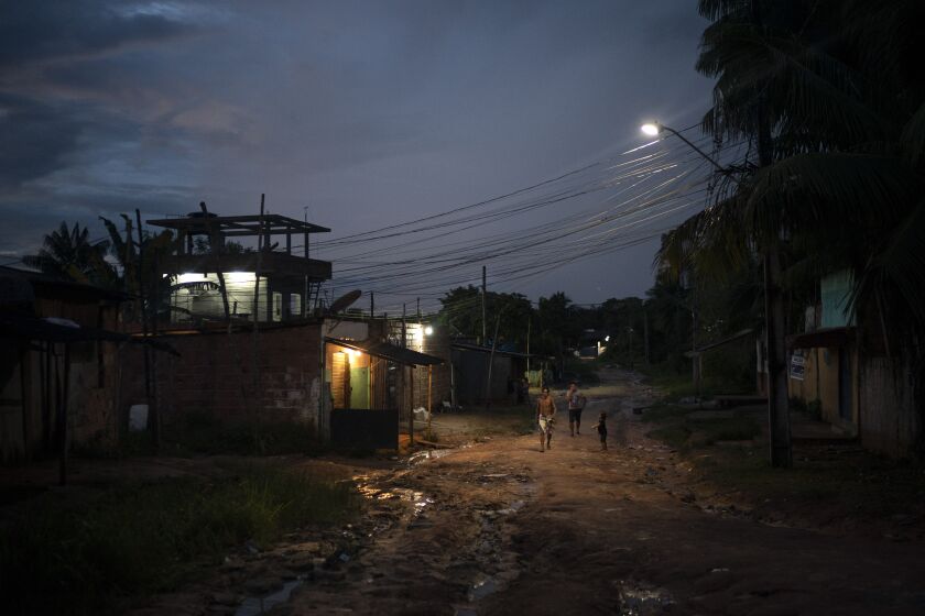 In this May 10, 2020 photo, residents walk on a dirt road in the Park of Indigenous Nations community, in Manaus, Brazil. The South American country has Latin America's highest COVID-19 death toll. The country's hardest hit major city per capita is in the Amazon — Manaus, where mass graves are filling up with bodies. (AP Photo/Felipe Dana)