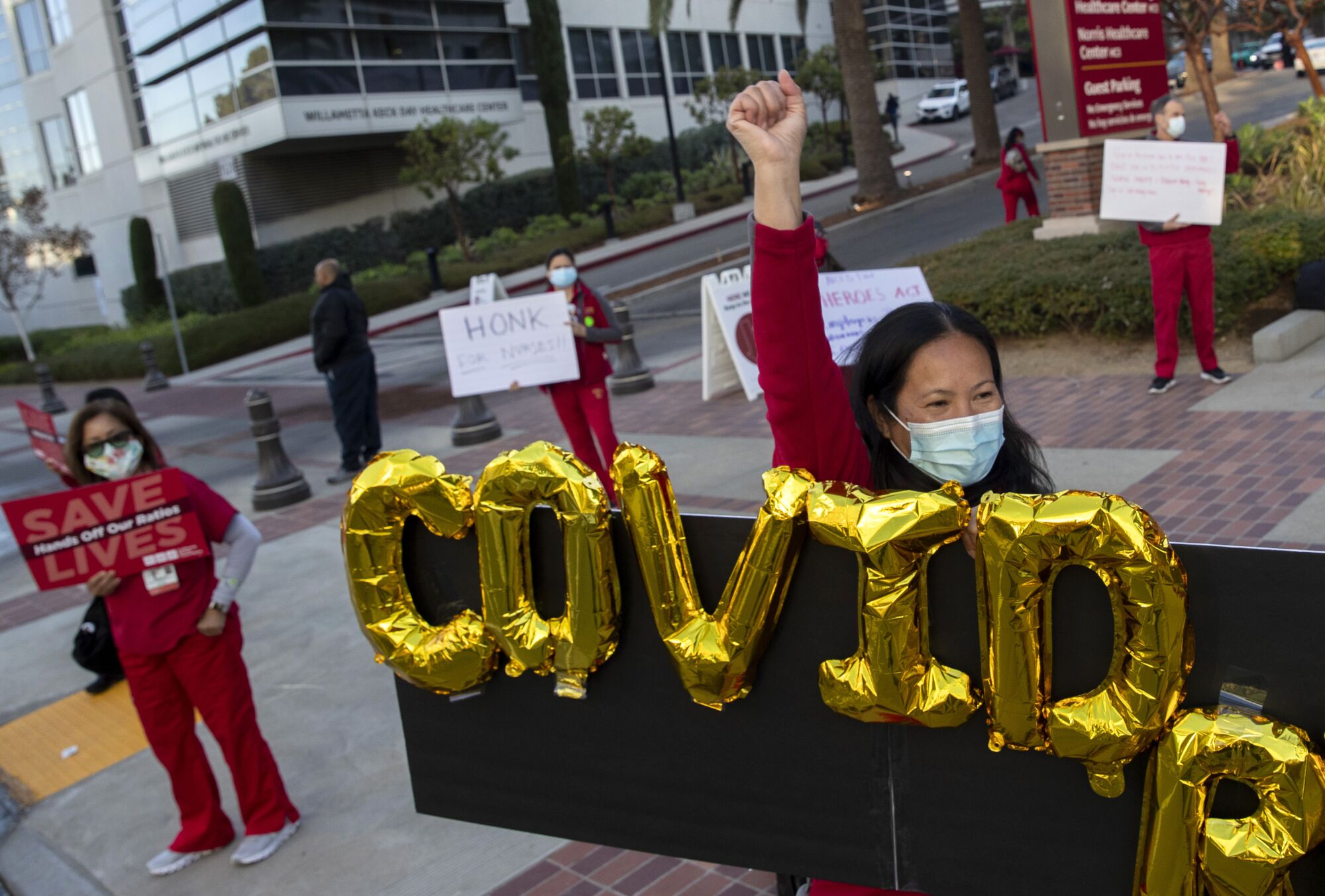 Next to mylar balloons that spell out "COVID," a protesting nurse raises a fist.