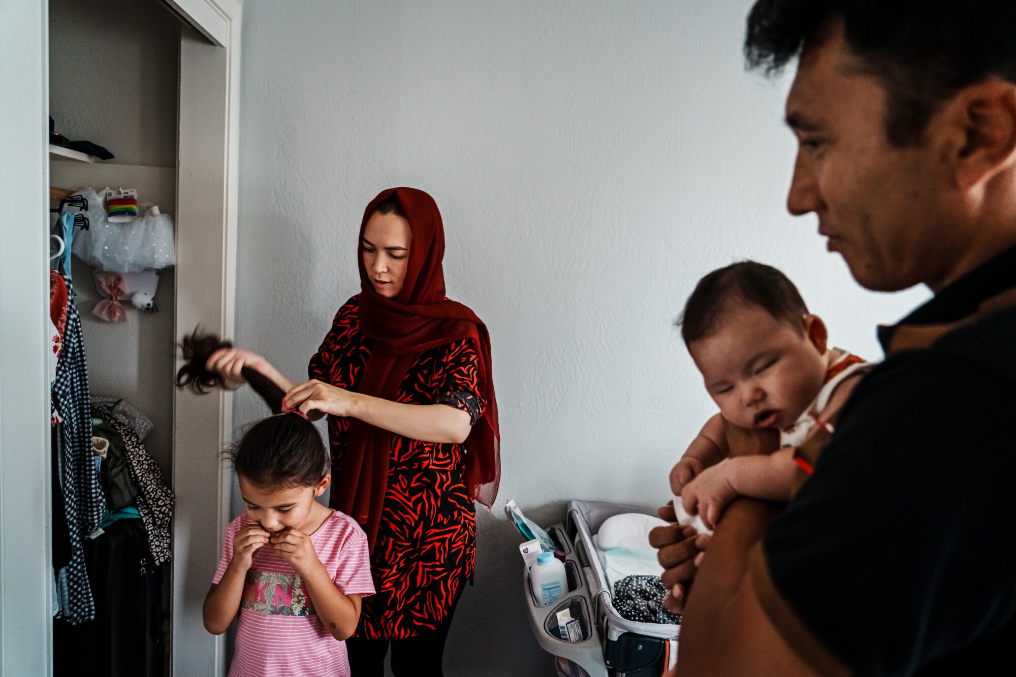 A year after the U.S. pullout from Afghanistan, refugees are still struggling to resettle 6 Mother braids hair of daughter while father is holding newborn baby.