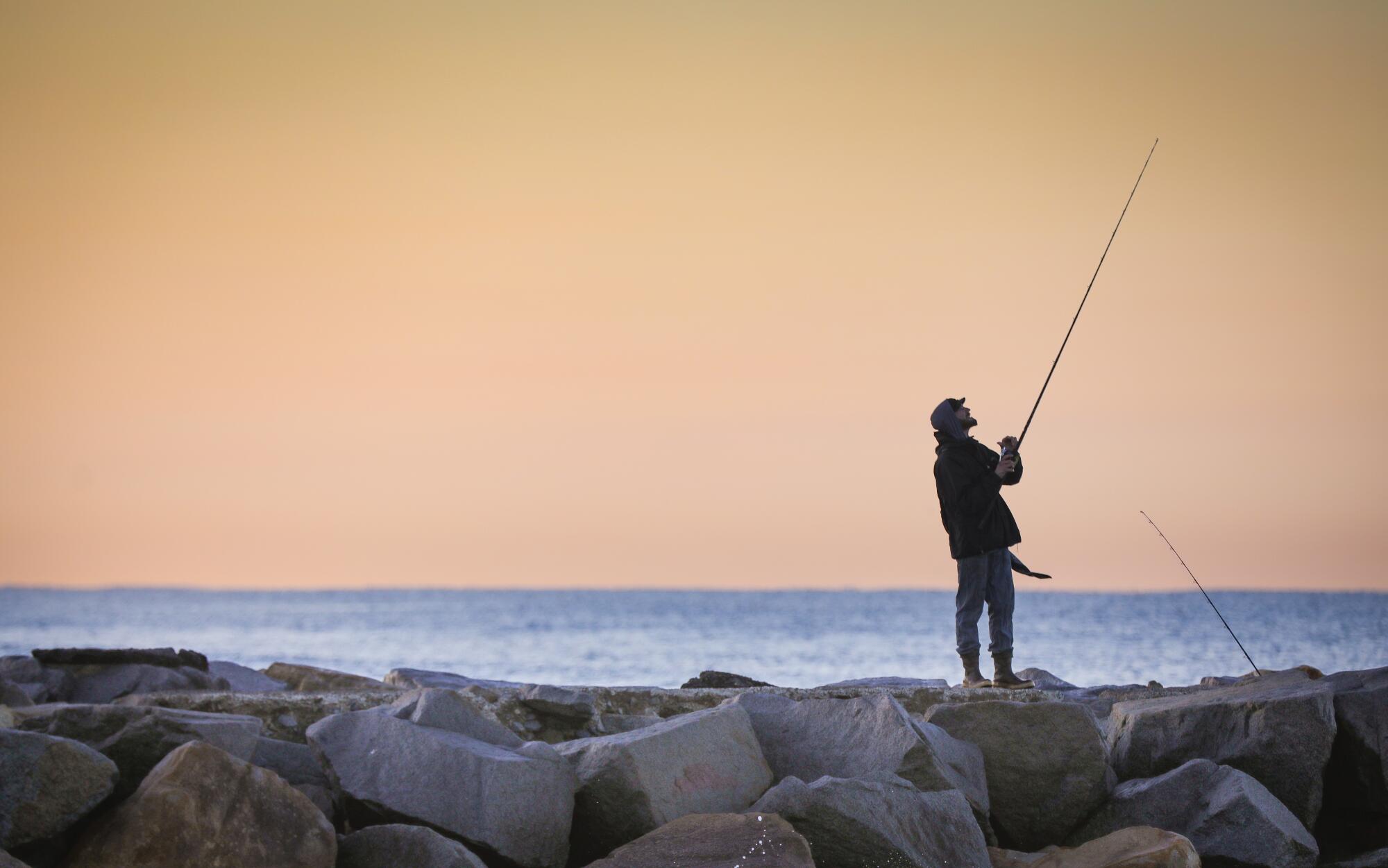 A fisherman casts out on a rock jetty near Oceanside Harbor Beach.