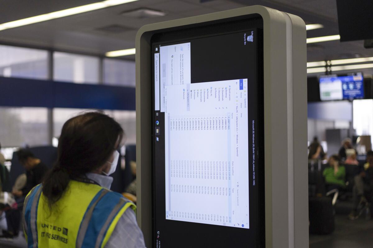Una técnico trabaja en un monitor de información cerca de la zona de embarque de United Airlines en el a