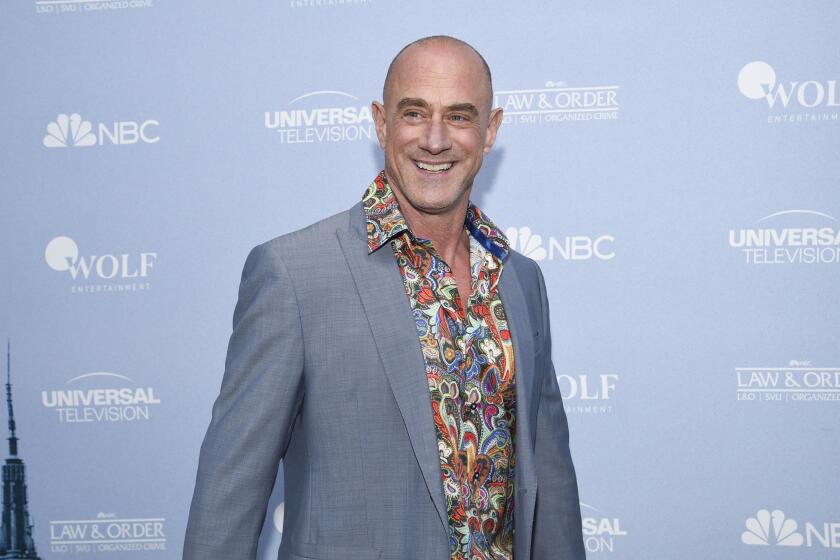 A bald man wearing a grey suit jacket and a colorful shirt smiles for pictures