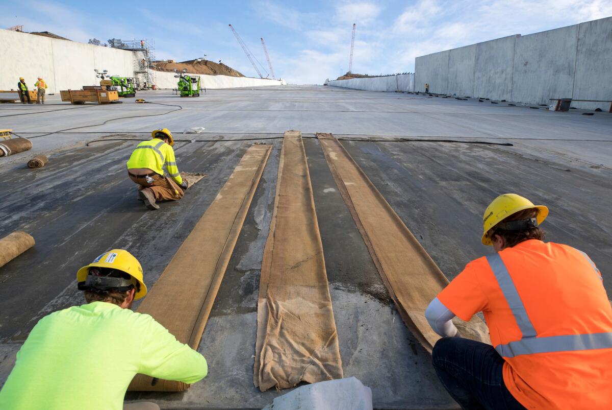 Workers roll up blankets used in the curing process for the structural concrete panels on the lower chute at the Lake Oroville flood control spillway on Monday.