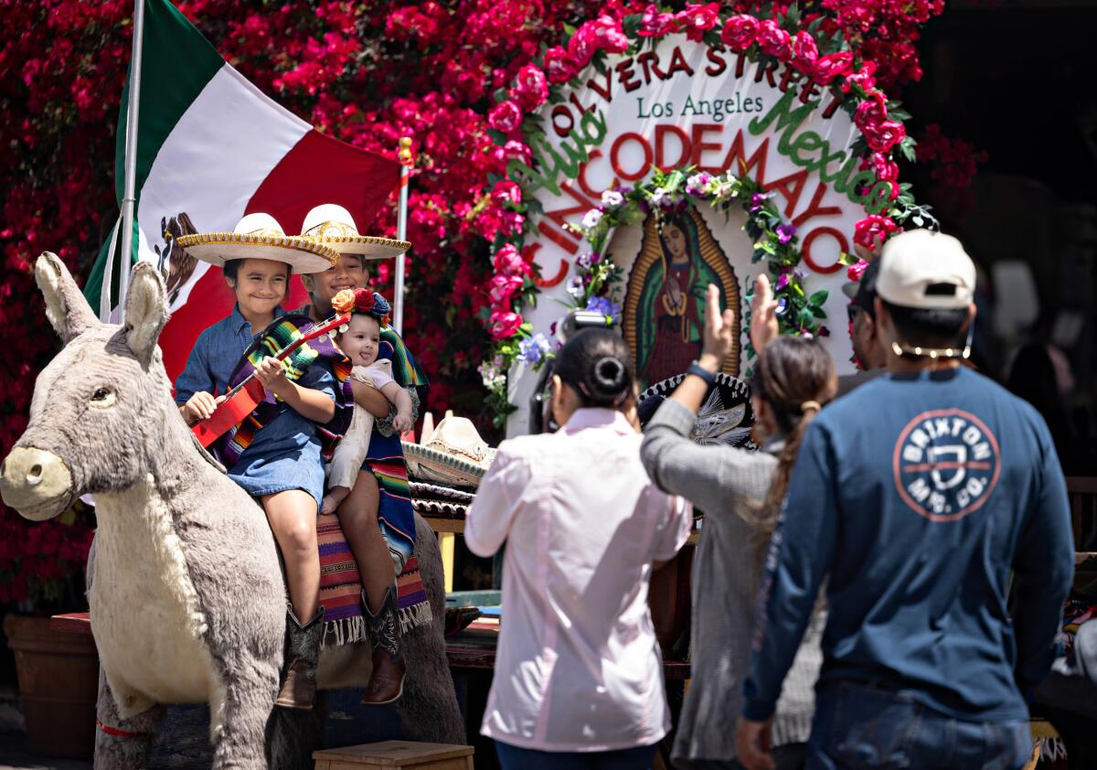 Children in sombreros pose for a photo on a stuffed donkey.