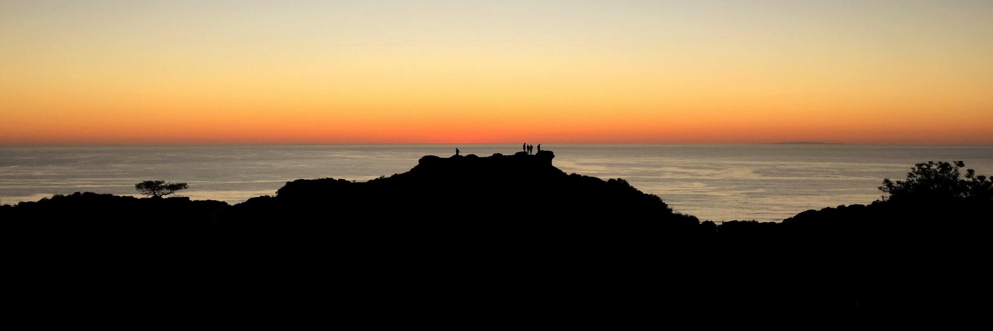 Torrey Pines State Natural Reserve with a silhouette of hills, and the ocean and orange sky behind them.
