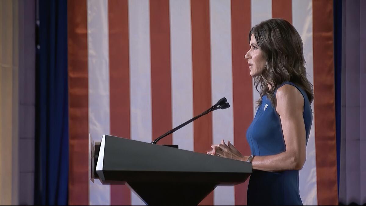 Governor Kristi Noem speaks with a flag as a backdrop