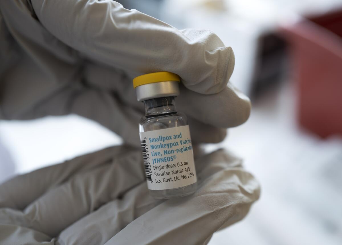 A gloved person holds a vaccine vial.