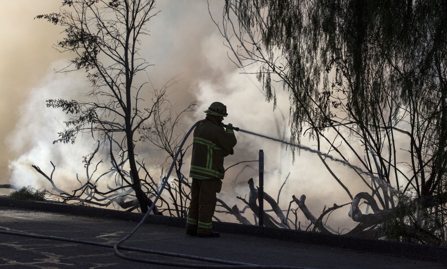 Los Angeles city firefighter Tony Acevedo puts water on a brush fire along the Woodley Ave. exit from the 118 freeway in Granada Hills.