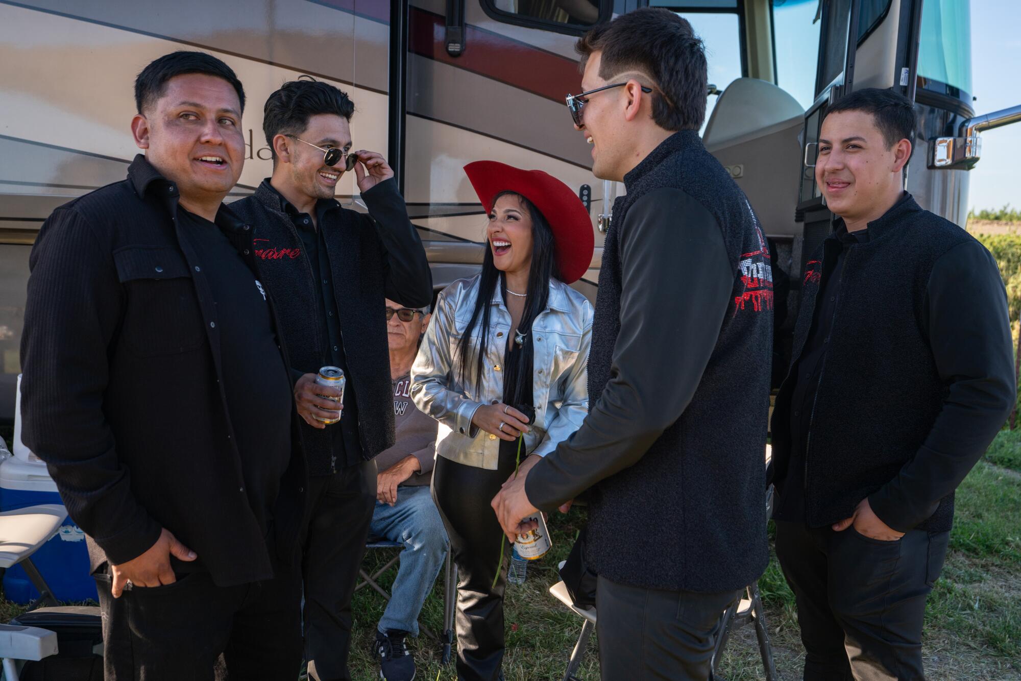 A woman wearing a silver top and men in black stand and smile near a tour bus. 