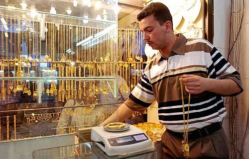 Muhammad Kamel, 28, weighs pieces of jewelry in his father's shop to calculate the price for customers, while window shoppers gazes at the showcase of jewelery outside.