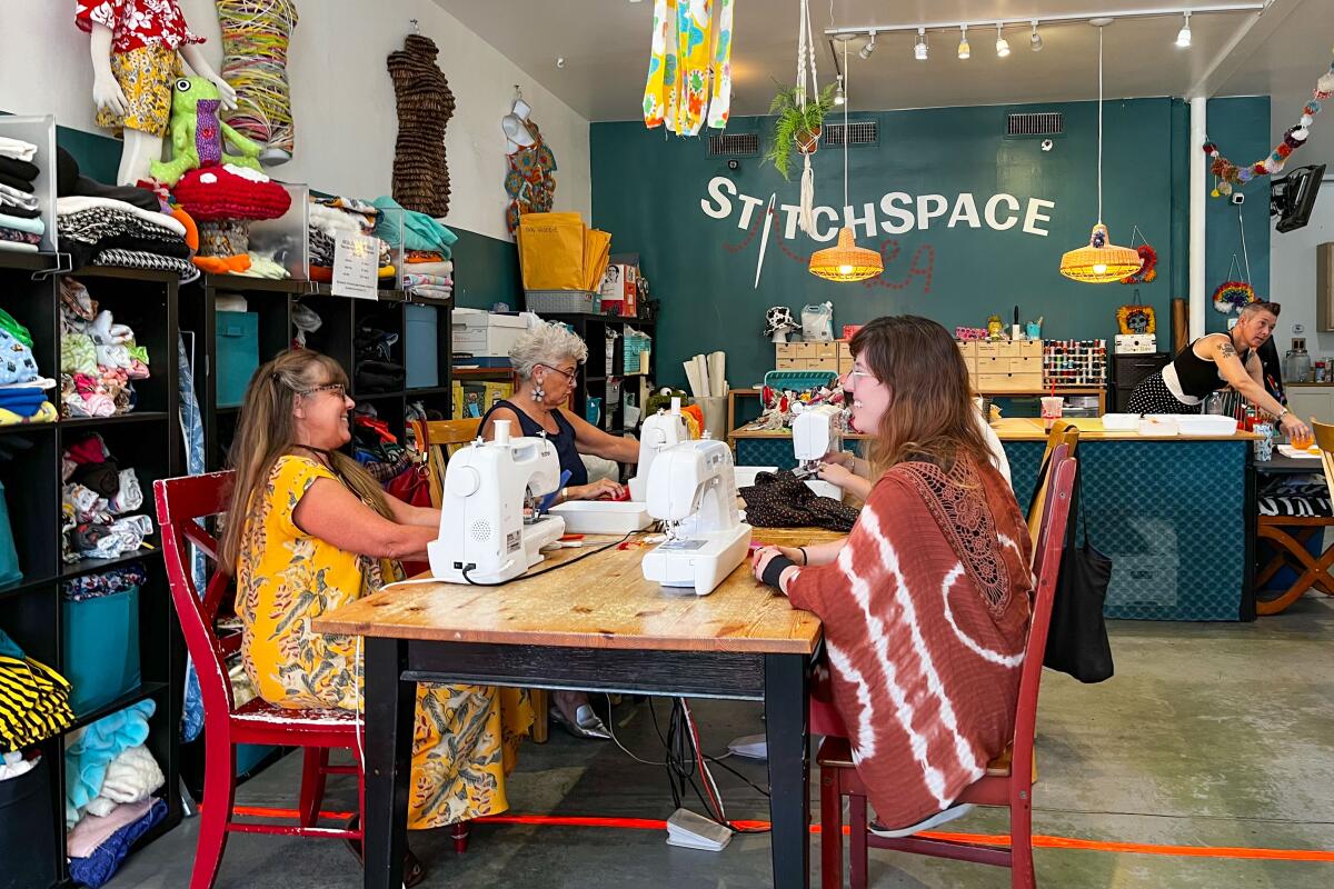 Women sitting around a table with sewing machines in a room that says StitchSpace on the wall