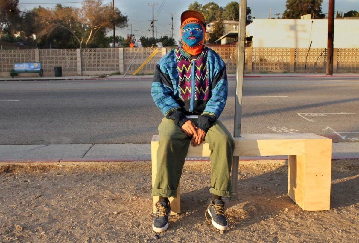 An anonymous artist poses on a freshly installed bench on Valley Boulevard near Soto Street in Los Angeles.