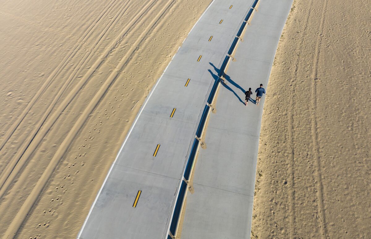 A couple running along a beach path on a bright day