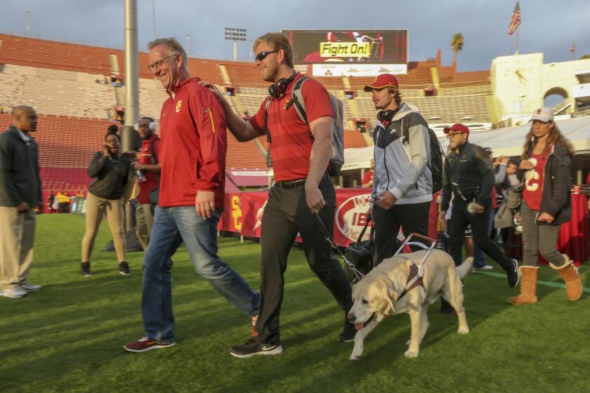 USC long snapper Jake Olson walks on a football field with the aid of his service dog, Quebec