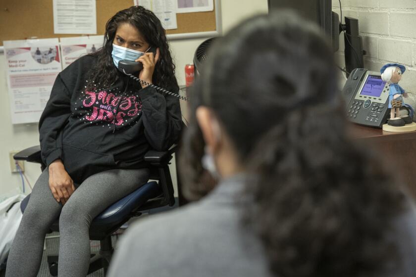 A woman wearing a medical mask holds a phone receiver in an office. 