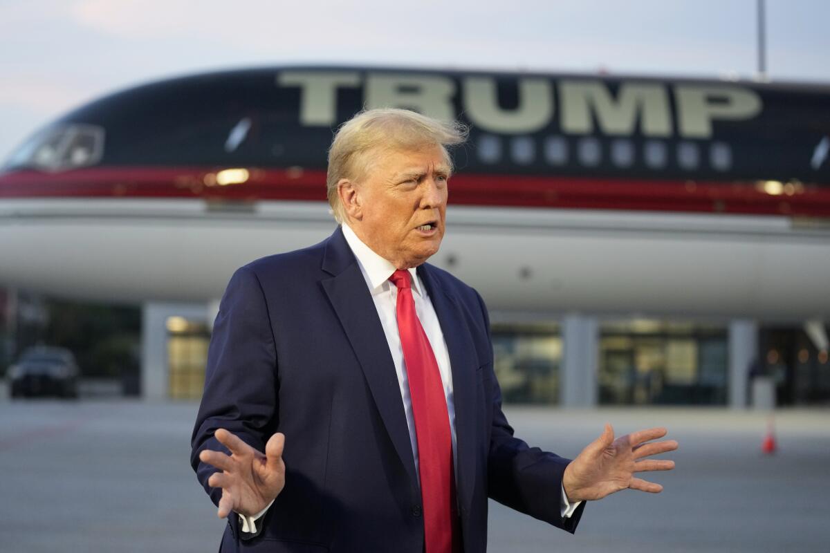 Former President Trump stand in front of a jetliner that says "TRUMP" on it